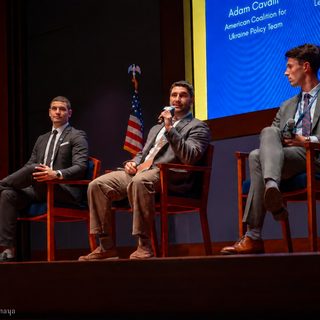 Closer view of the three panelists, the middle panelist speaking into a microphone